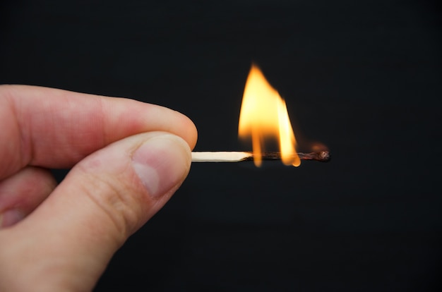 closeup of burning match in hand on black.