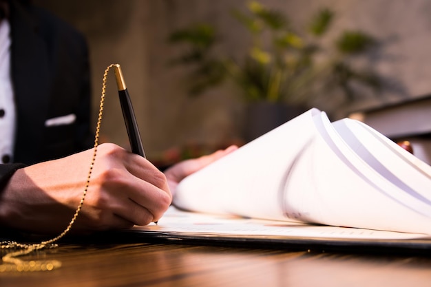Крупный план бизнес-ручной подписи документов для утверждения соглашения с партнерами, работающими на ноутбуке на столе в современном офисе