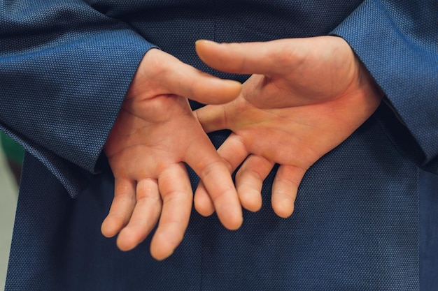 Closeup of a business man with his hands behind his back and\
fingers crossed torso and hands only man is unrecognizable