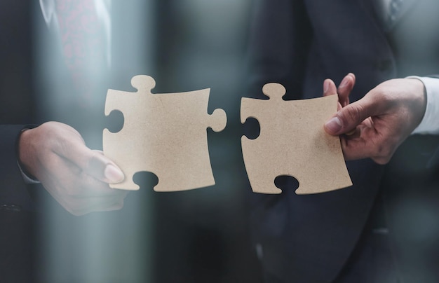 Closeup Of Business Partners Combining Two White Puzzle Pieces On Black Background