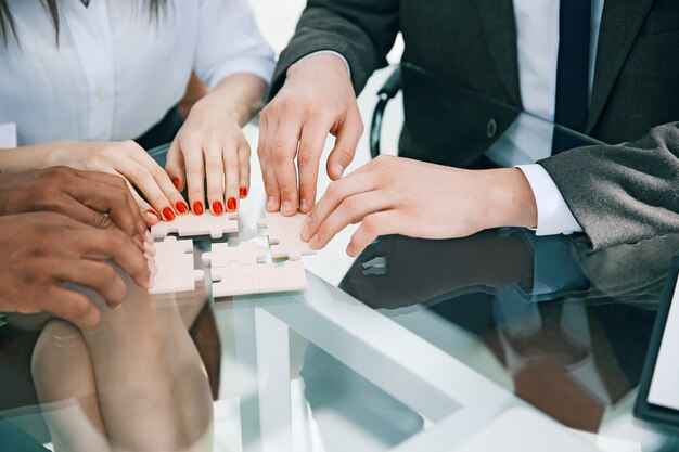 Primo piano .business team assemblaggio puzzle seduto dietro una scrivania .il concetto di strategia negli affari