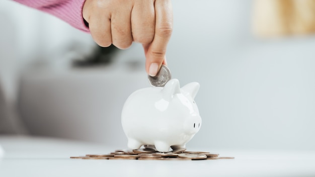 Closeup of business woman hand putting money coin into piggy bank for saving money. saving money and financial concept