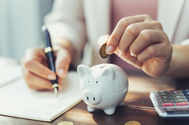 Closeup of business woman hand putting money coin into piggy bank for saving money saving money