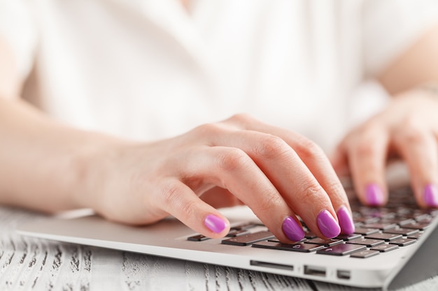 Foto primo piano della mano della donna di affari con il manicure che scrive sulla tastiera del computer portatile