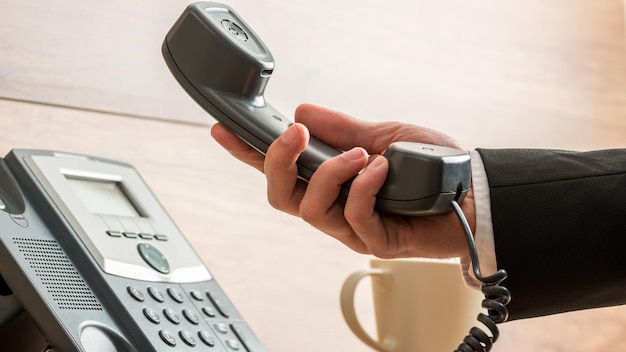 Closeup of businessman holding handset of a black landline telephone