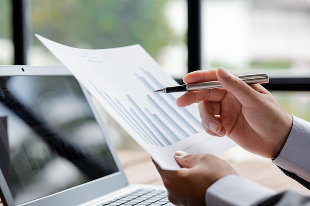 Closeup businessman holding a pen and pointing at a bar chart\
on a company financial document he is analyzing historical\
financial data to plan how to grow the company financial\
concept