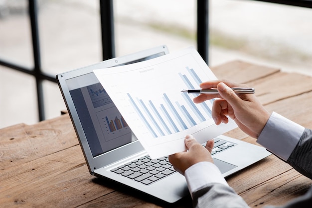 Closeup businessman holding a pen and pointing at a bar chart on a company financial document he is analyzing historical financial data to plan how to grow the company Financial concept