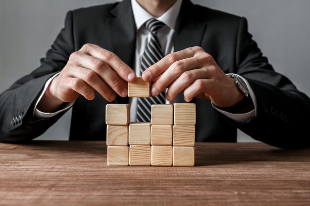 Closeup of businessman making a structure with wooden cubes. Success and business strategy concept.