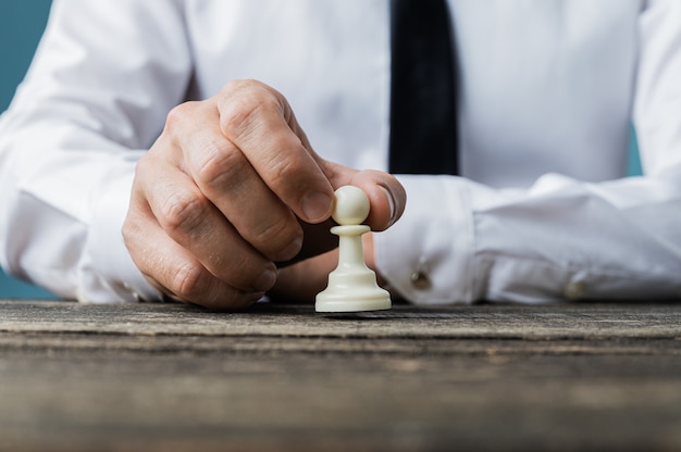 Closeup of businessman placing white pawn chess piece on rustic wooden desk in a conceptual image.