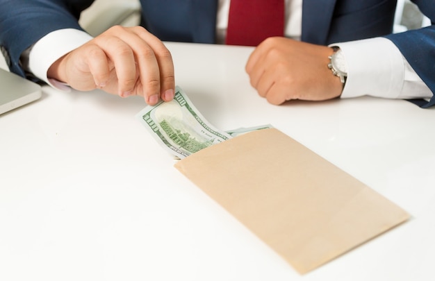 Closeup businessman pulling banknote out of envelope lying on table