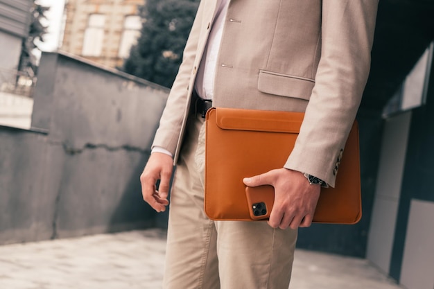 Photo closeup of businessman with brown leather cases of laptop and phone