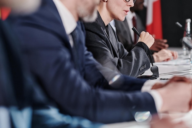 Closeup of businesswoman giving a speech in microphone while sitting at table with her colleagues