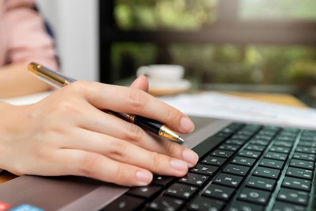 オフィスデスクでノートパソコンにペンを持つ実業家の手の拡大。