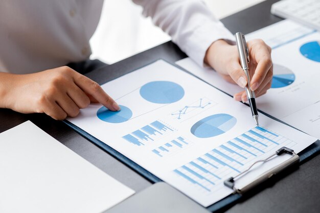 企業の財務情報シートの棒グラフを指すペンを持っているクローズアップの実業家の手実業家は、財務部門から提供された財務情報を調べます