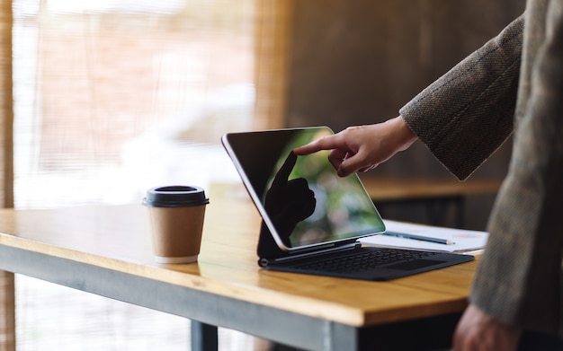 Closeup  of a businesswoman touching and pointing finger at digital tablet screen as a computer pc with coffee cup and paperwork on the table