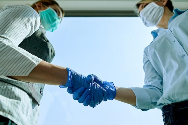 Closeup of businesswomen shaking hands while wearing protective gloves during coronavirus pandemic
