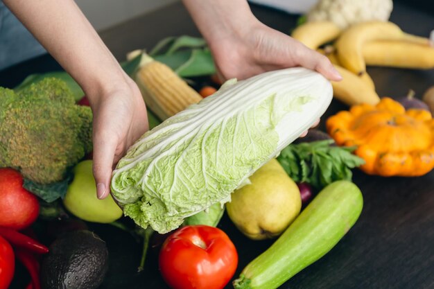 Closeup cabbage in a woman's hand on the kitchen table among vegetables