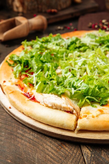 Closeup on caesar pizza with chicken and iceberg salad on the wooden table