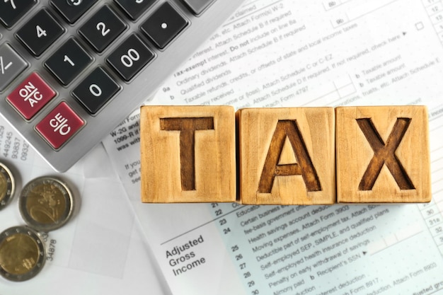 Closeup of calculator documents and wooden blocks with word TAX on table