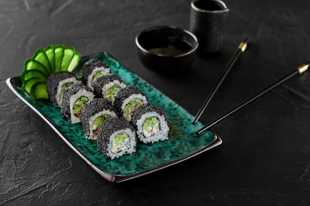 Closeup of California rolls in black tobiko caviar with filling of tiger prawn, avocado, cucumber and japanese mayonnaise traditionally served with soy sauce . Authentic food concept