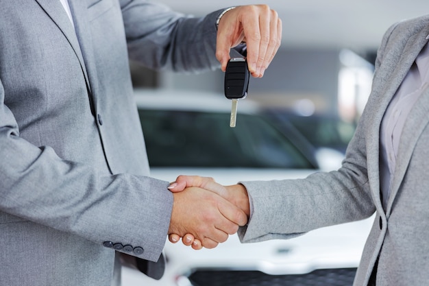 Foto primo piano del venditore di auto stringe la mano al cliente e consegna le chiavi della macchina mentre si trovava nel salone dell'auto