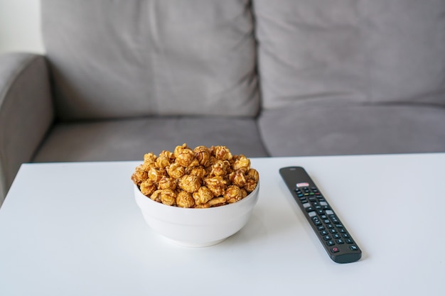 Closeup of caramel popcorn, remote control for smart TV. Watching a movie on sofa at home concept.