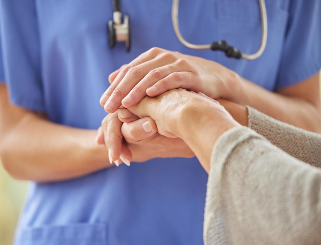 Closeup of caring nurse comforting senior patient in old age home Zoomed in unknown elderly woman being supported touching and holding a medical aids hand Elderly woman bonding with her caregiver