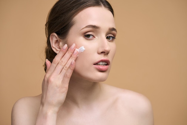 Closeup Caucasian young woman with healthy glowing clear skin applying moisturizer on her face