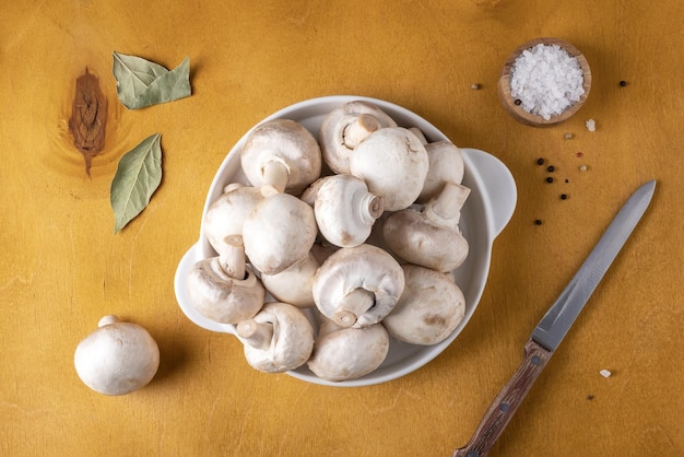 Closeup of champignon mushrooms on a white ceramic plate on a yellow background Selective focus