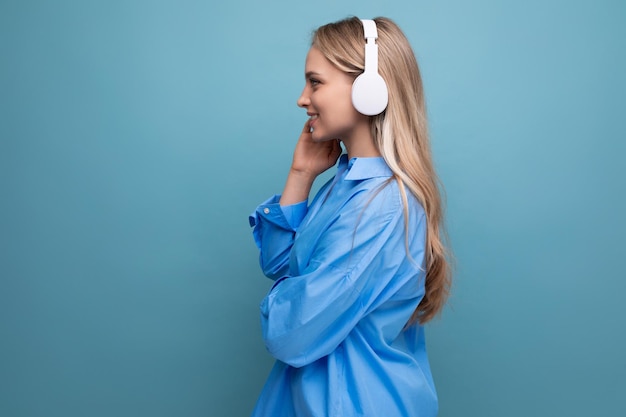 Closeup charming girl with pleasure listening to a podcast in big headphones on a blue isolated