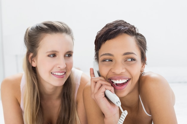 Closeup of cheerful female friends using phone in bed