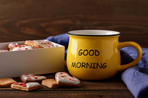 Closeup cheerful morning with yellow Cup of coffee or tea with box of cookies hearts on wooden background, good morning concept