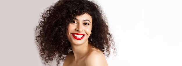 Closeup of cheerful smiling woman with red lipstick and curly hairstyle looking happy standing over