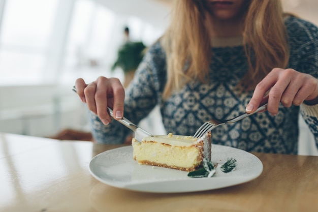 Closeup of cheesecake and leaf of mint sprinkled powder sugar on white plate.