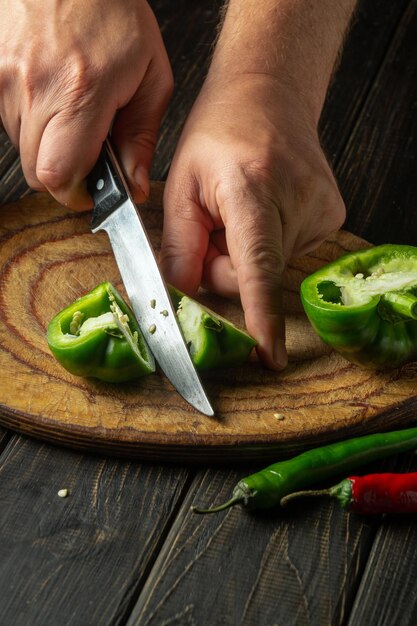 Closeup of a chef hands cutting green peppers on a cutting board