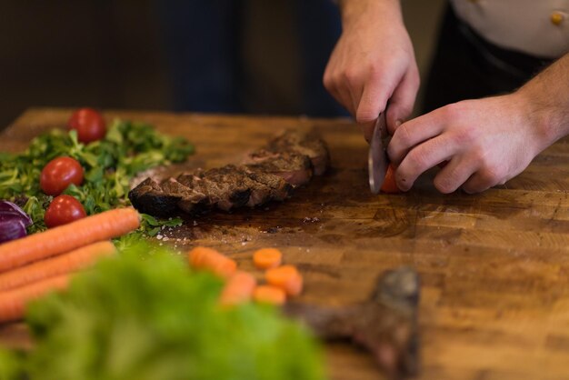 closeup of Chef hands in hotel or restaurant kitchen preparing beef steak with vegetable decoration