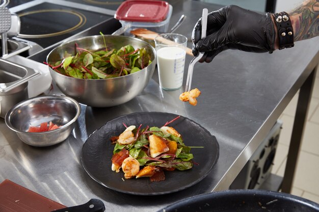 Крупным планом руки шеф-повара готовят салат из креветок на кухне роскошного ресторана