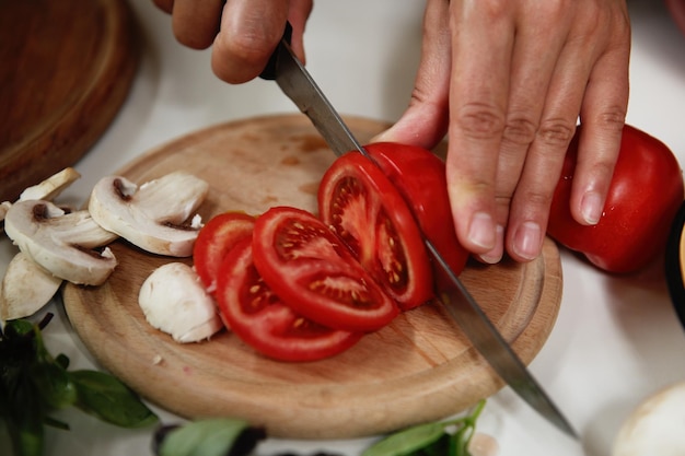 写真 クローズ アップ シェフ手健康的なビーガン フードを準備しながら木製のまな板に熟したジューシーなトマトをスライス