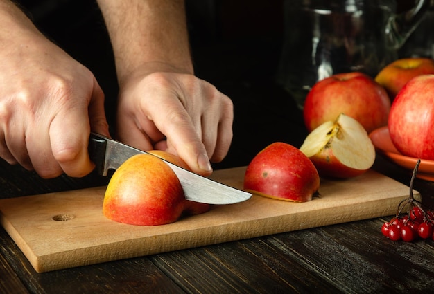 Foto primo piano delle mani di uno chef con un coltello che affetta le mele su un tagliere di legno per preparare deliziose bevande alla frutta l'idea della dieta delle mele copia spazio