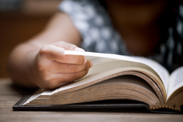 Closeup child hand opening and reading a book in library in vintage color tone 