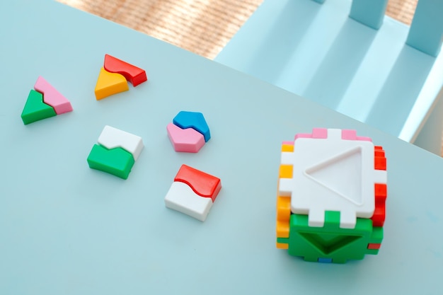 Il primo piano delle mani del bambino raccoglie il sorter di puzzle cubo con forme geometriche inserite e blocchi di plastica colorati