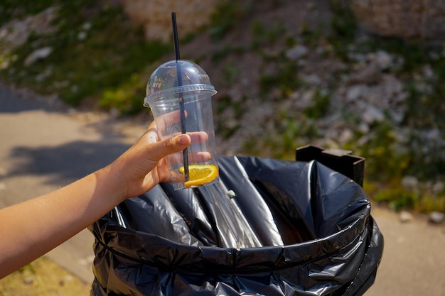 Closeup children hand throwing empty plastic cup in garbage bag