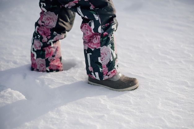 冬のスーツで子供の足のクローズ アップ フェルトのブーツで雪の中を歩く少女の足の側面図 降雪後の凍るような晴れた日に冬に歩く