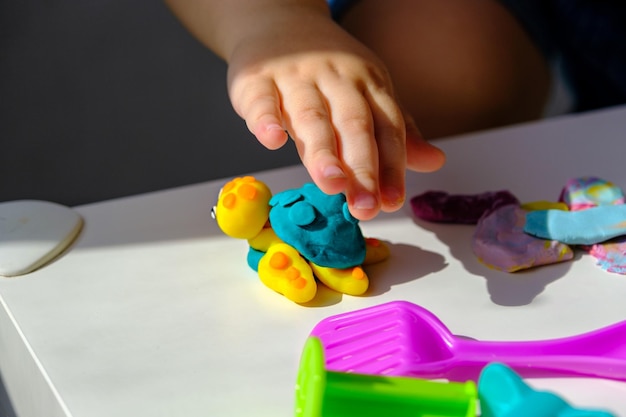 흰색 탁자에 플라스틱 거북이가 있는 닫혀 있는 어린이 손은 가정에서 플라스틱으로 만든 창의적인 게임입니다
