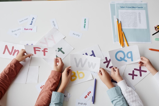 Photo closeup of children sitting at the table together with cards and learning english alphabet