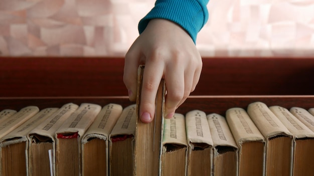 Близкий взгляд на руку ребенка, берущего книгу с книжной полки