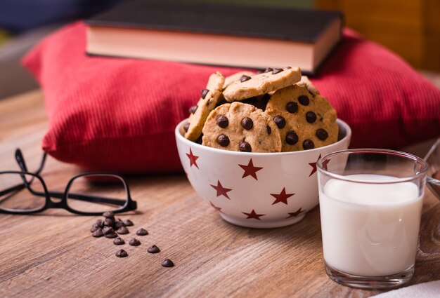 Closeup of chocolate chip cookies on stars bowl and milk glass over a wooden background