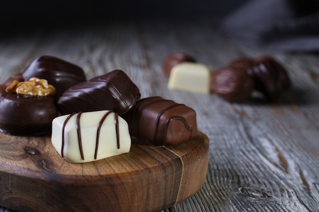 Closeup of Chocolates in different shapes and colors on a chopping board, placed on a dark rustic wooden table
Copy space