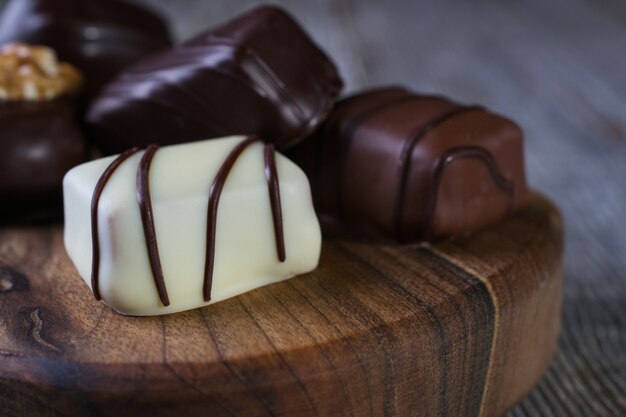 Closeup of Chocolates in different shapes and colors on a chopping board, placed on a dark rustic wooden table