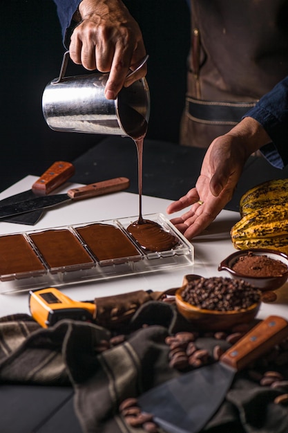 Photo closeup of the chocolatier's hands pouring chocolate into the molds